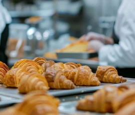 Freshly baked croissants arranged on trays in a busy bakery kitchen
